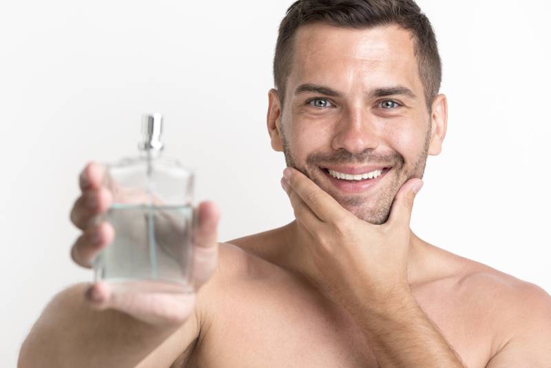 Homem sem camisa com mão no queixo segurando frasco de perfume