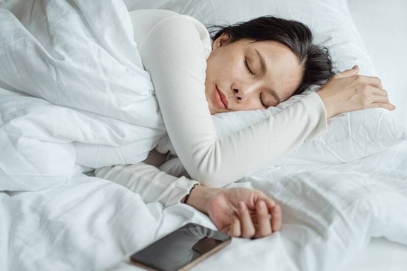 Mulher asiática dormindo ao lado de celular com roupas de cama branca