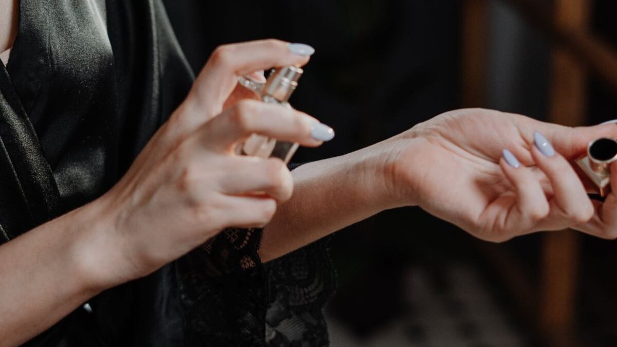 Las manos una mujer aplicándose perfume en las muñecas