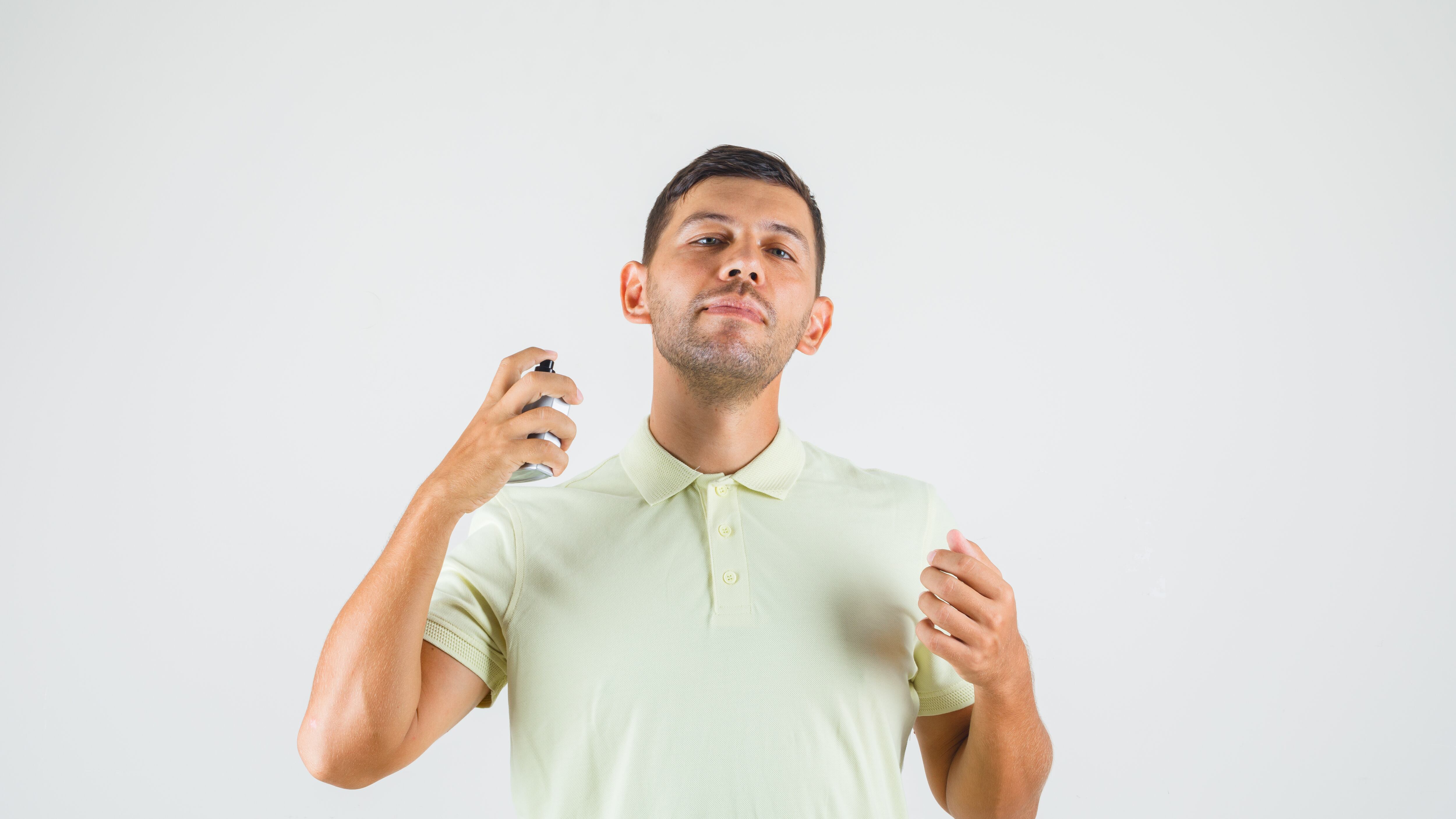 Young man applying perfume on his neck in t-shirt front view.